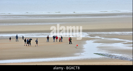 I turisti con ombrelloni passeggiate sulla spiaggia lungo la costa del Mare del Nord in località balneare in un giorno di pioggia durante le vacanze estive Foto Stock