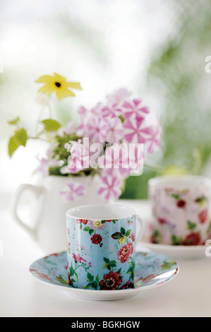 Motivi floreali e teacups piattini con fiori in una brocca Foto Stock