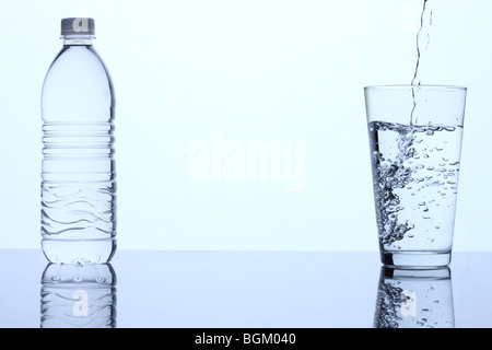 Bottiglia di acqua e un bicchiere di acqua essendo riempito Foto Stock