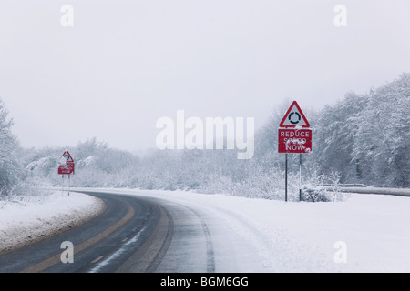 Strada con il ridurre la velocità adesso firma durante la caduta di neve dell'inverno 2010 Foto Stock