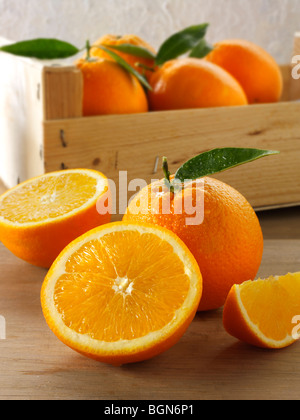 Arance fresche intere e tagliare metà con foglie in una scatola Foto Stock