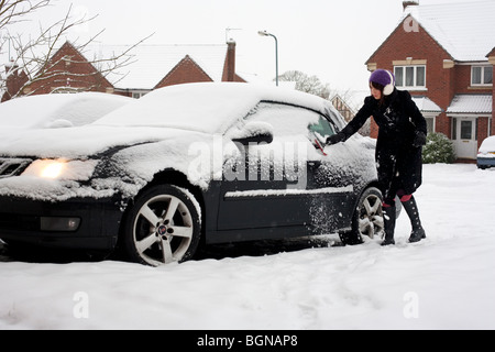 Una donna la rimozione di neve dalla sua auto sulla sua strada in Worcestershire, Regno Unito Foto Stock