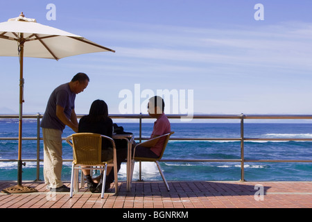 Giovane a un tavolo sulla spiaggia sotto un ombrellone Foto Stock