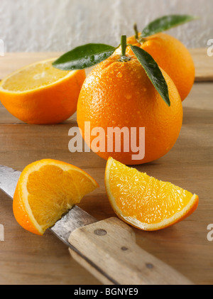 Intero e tagliare le arance fresche con foglie in una cucina Foto Stock