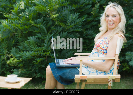 Ritratto di una donna matura seduti in poltrona e utilizzando un computer portatile Foto Stock