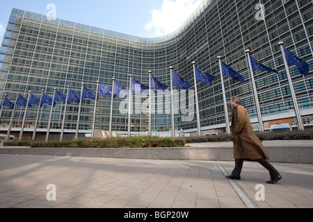 Un uomo cammina accanto alla bandiere europee al di fuori dell'edificio Berlaymont, la sede centrale della Commissione europea a Bruxelles Foto Stock