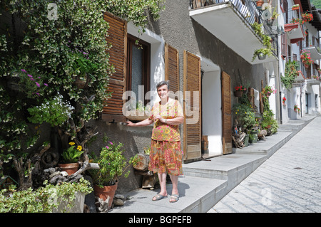 Casa orgogliosa lady fuori il suo piatto con fiori scatole di finestra di scalatori in stretta strada Pont St Martin Valle d'Aosta Italia Foto Stock