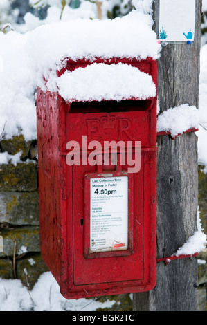 Rusty post box in un villaggio inglese, coperto di neve Foto Stock