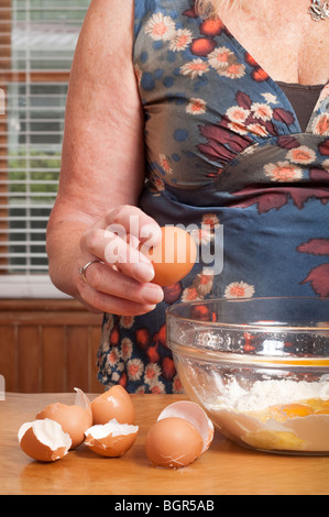 Le donne le uova di cracking nel recipiente di miscelazione di farina con le uova guscio accanto alla ciotola Foto Stock