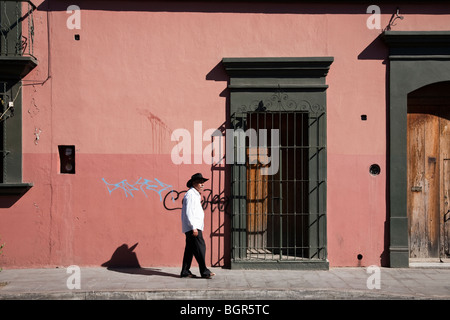 Il vecchio uomo con baffi bianchi vestita di nero sombrero passeggiate passato coloniale bellissimo edificio rifinito con rosa luminoso intonaco Foto Stock