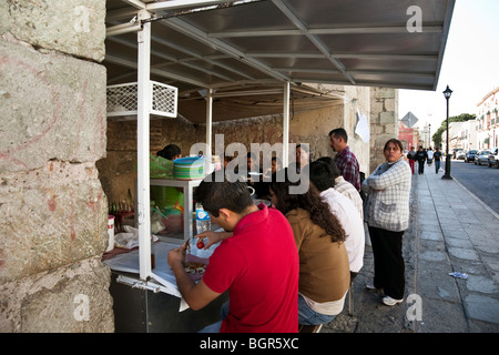 Seduti ai clienti di godere il loro cibo mentre quelli in linea attendere per la loro cucina tacos ad una bancarella di strada booth città di Oaxaca Messico Foto Stock