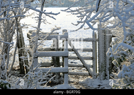 Coperta di neve sentiero pubblico con kissing gate entrando in campo gli agricoltori Foto Stock