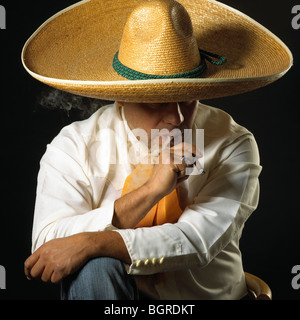 Un uomo messicano che indossano il tradizionale hat, un sombrero, e fumare un sigaro. Foto Stock