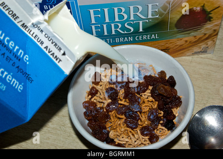 Versare il latte scremato oltre una sana ad alto contenuto di fibre di crusca di cereali per la prima colazione di uvetta Foto Stock