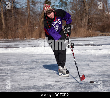 Ragazzo adolescente giocare ad hockey su un laghetto congelato Foto Stock