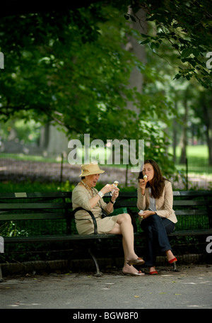 Due donne condividono gelato e amicizia su una panchina di Central Park di New York City. Foto Stock