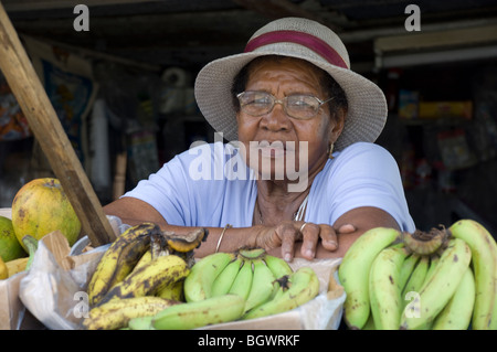 Una donna la vendita delle banane a una pressione di stallo stradale; Santa Lucia, le isole Windward Caraibi Foto Stock