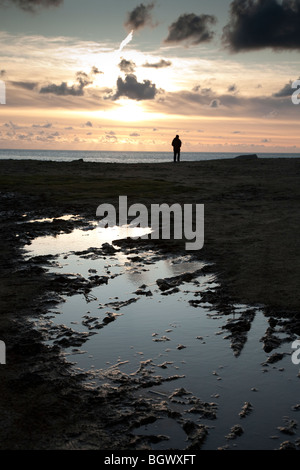 Un uomo si affaccia al mare al sole di setting da Portland Bill, Weymouth Dorset, Regno Unito Foto Stock