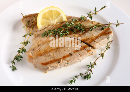 Una grigliata di bistecca di tonno, guarnita con rametti di timo, su una piastra con un cuneo di limone Foto Stock