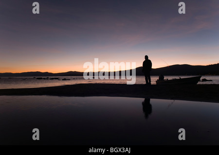 Una silhouette di un pescatore e la sua piccola barca sulla riva del lago di Tahoe durante il tramonto in California Foto Stock