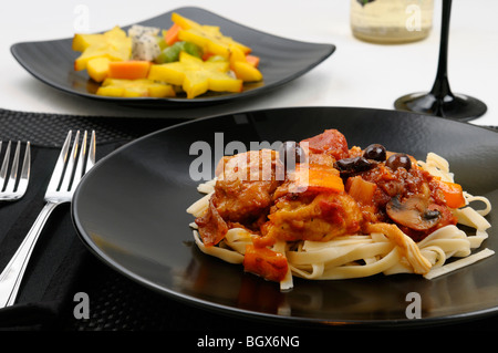 Close up di messa in tavola con piatto di Pollo alla Marengo con insalata di frutta e vino bianco Foto Stock