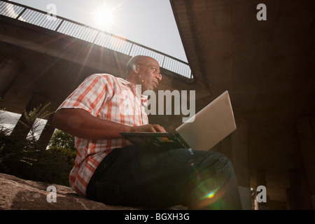 Uomo al lavoro su laptop in città Foto Stock