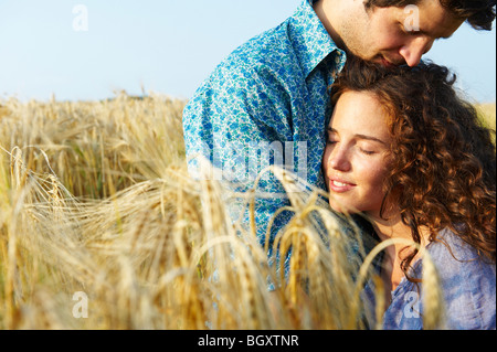Giovane seduto in un campo di grano, sorridente Foto Stock