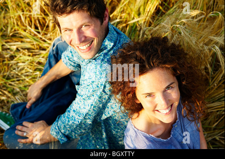 Giovane seduto in un campo di grano, sorridente Foto Stock