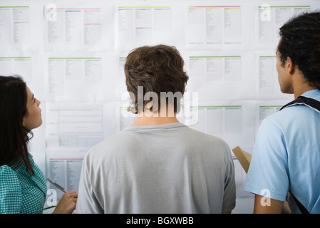 Studenti del college controllo bulletin board per le assegnazioni in aula, vista posteriore Foto Stock