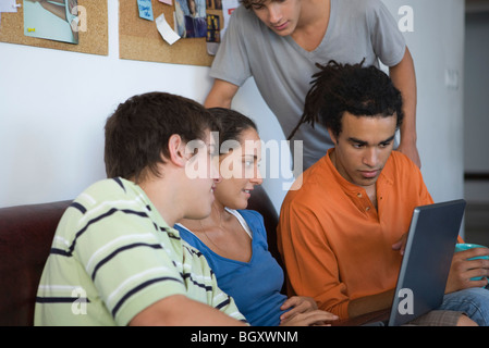 Gli studenti universitari riuniti attorno a un compagno di classe utilizzando il computer portatile Foto Stock