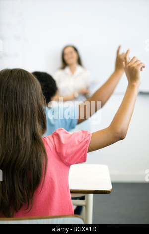 Gli studenti della scuola elementare alzando la mano in classe, vista posteriore Foto Stock