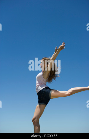 Giovane donna con le braccia sollevate, in equilibrio su una gamba Foto Stock