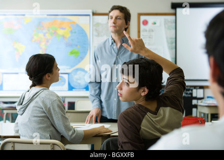 Studente di scuola superiore alzando la mano in classe, guardando sopra la spalla Foto Stock