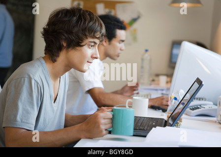 Studente di College utilizzando computer portatile, una tazza di caffè in mano Foto Stock