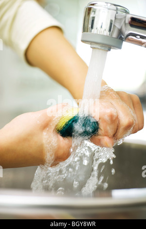 Persona spugna di risciacquo sotto il rubinetto di cucina Foto Stock