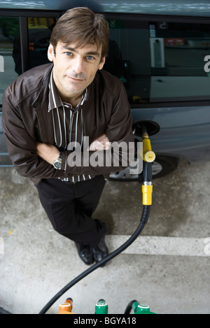 Uomo in piedi con le braccia incrociate il rifornimento di carburante il veicolo a gas station Foto Stock