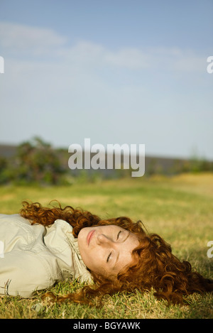 Giovane donna con gli occhi chiusi che giace sul retro in campo erboso Foto Stock