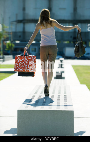 Donna che cammina su una panchina nel parco il trasporto delle borse della spesa, vista posteriore Foto Stock