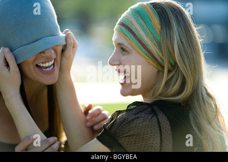 Donna scherzosamente tirando amico del Berretto in maglia verso il basso sopra i suoi occhi Foto Stock