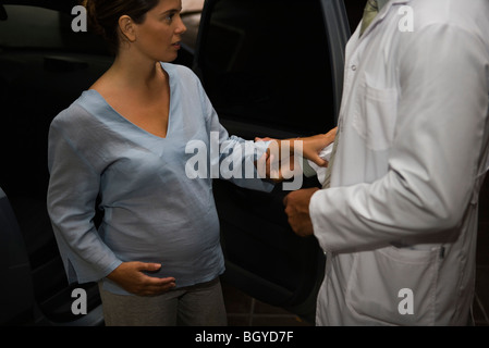 Medico aiutare la donna incinta al di fuori della vettura, ritagliato Foto Stock