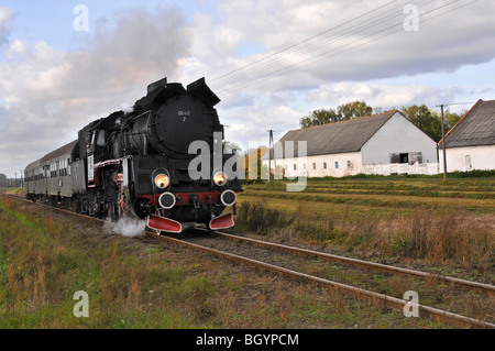 Locomotiva a vapore sotto il vapore che viaggiano attraverso la campagna polacca in prossimità di edifici agricoli Foto Stock