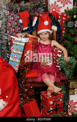 Poco ragazza seduta in Santa's chair circondato da regali di Natale e regali Foto Stock