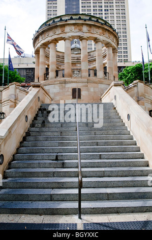 ANZAC War Memorial Brisbane Australia | BRISBANE, Australia - Una scalinata di granito sale verso il santuario colonnato dell'ANZAC War Memorial, fiancheggiata dalla bandiera Union Jack e della nuova Zelanda in ANZAC Square. Diciotto colonne doriche circondano la rotonda, un numero scelto per segnare il 1918, l'anno in cui si concluse la prima guerra mondiale. La trablatura nomina battaglie sul fronte occidentale, tra cui Amiens e Ypres, dove le truppe australiane e neozelandesi combatterono. Foto Stock