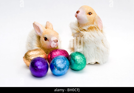 Due ornamenti di coniglio con una piccola selezione di coloratissimi mini uova di pasqua di cioccolato su uno sfondo bianco Foto Stock