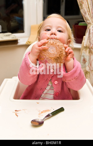 Chiudere verticale su ritratto di una bambina di salire in un pasticcio di mettere la sua coppa di gelato al cioccolato sulla sua testa Foto Stock