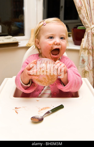 Chiudere verticale su ritratto di una bambina di salire in un pasticcio di mettere la sua coppa di gelato al cioccolato sulla sua testa Foto Stock