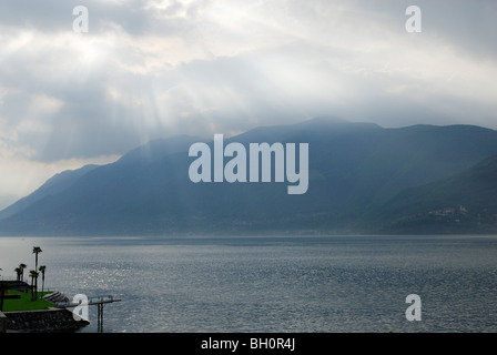 Raggi di sole che splende attraverso le nuvole sopra il lago Maggiore, lido con palme, Brissago, Lago Maggiore, Lago Maggiore, Ticino, Foto Stock