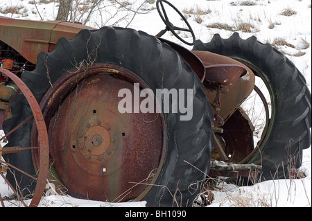 Questo vecchio trattore abbandonati si siede sul bordo di un campo accanto a un vecchio rastrello fieno entrambi ow che sono destinati alla ruggine di distanza. Foto Stock