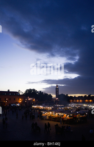 La folla presso le bancarelle del mercato in Piazza Jemaa El Fna dopo il tramonto Marrakech Marocco. La Moschea di Koutoubia in distanza. Foto Stock