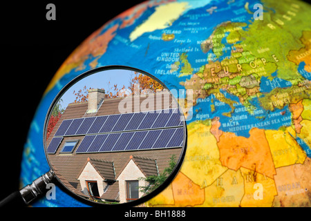 Pannelli solari fotovoltaici / celle sul tetto di casa vista attraverso la lente di ingrandimento tenuto contro illuminato globo terrestre Foto Stock